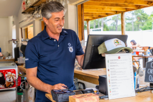 personne souriante à la caisse de l'établissement pour partager la belle humeur des jours de vacances avec les résidents saisonniers