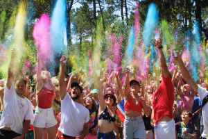 Groupe de participants en tenue colorée sautants lors d'une course Color Run, avec des poudres de couleurs vives en suspension dans l'air, sous un ciel ensoleillé, célébrant la joie et la fête