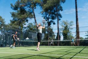 service d'une jeune femme au padel contre deux adversaires hommes par temps ensoleillé lors d'un tournoi organisé lors des vacances d'été au bord de mer dans les landes