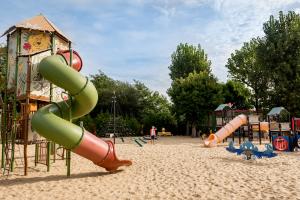 Aire de jeux pour enfants de 5 à 12 ans située dans un parc au camping, comprenant diverses infrastructures de jeux colorées telles que des toboggans, des balançoires, des structures d'escalade et des modules de jeux, le tout installé sur un sol en sable pour assurer la sécurité, avec des espaces verts et des arbres en arrière-plan
