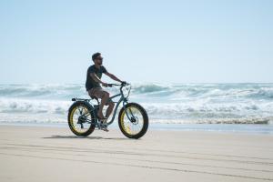 Homme pédalant sur un vélo fatbike de location le long de l'océan, sur une plage de sable doré près des pins, au meilleur camping des Landes en bord de mer, profitant d'une balade sportive et d'un paysage naturel exceptionnel.