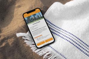 Mockup d'un téléphone sur une serviette de bain posée sur la plage dans le sable avec un coquillage et l'écran qui montre la fiche de réservation des courts de padel pour disputer un match avec ses amis, sa famille ou d'autres vacanciers