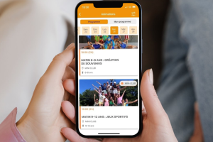Photo d'une maman et de sa fille tenant un téléphone mobile ensemble, souriantes, en train de consulter le planning des animations du mini club sur l'application mobile du camping, illustrant la planification des activités pour enfants