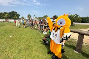 La mascotte Soly qui encourage les campeurs footballers au terrain verduré de gazon par un joli temps ensoleillé 