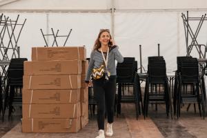 Femme souriante au téléphone dans un bureau, organisant activement un séminaire d’entreprise pour en assurer la réussite, entourée de matériel de travail et de cartons