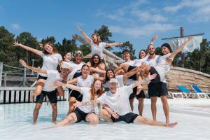 Photo de groupe des animateurs du camping Le Vieux Port saison 2025, posant souriants et en tenue décontractée au parc aquatique, entourés de structures aquatiques colorées, toboggans et bassins, sous un ciel clair d’été.