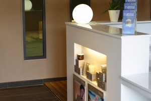 Vue accueillante de l’entrée de l’espace bien-être du camping : porte vitrée et moderne, panneau d’indication spa et bien-être, chemin dallé entouré de plantes vertes et fleurs, lumière naturelle, ambiance sereine et élégante invitant à la détente dès l’arrivée.