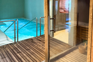 Vue intérieure lumineuse et élégante d’un spa moderne, présentant un sauna en bois avec bancs accueillants, un hammam aux parois carrelées et à la vapeur diffusée sur la droite, ambiance sereine et relaxante avec lumière tamisée, décoration zen, serviettes et accessoires de bien-être à disposition.