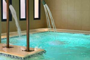 Vue intérieure du spa du camping, comprenant une piscine chauffée avec jets d’eau massants, bain à remous, éclairage tamisé créant une atmosphère relaxante, zone de repos avec transats, décor élégant, vapeur légère au-dessus de l’eau et ambiance apaisante, idéale pour la détente et le bien-être aquatique.