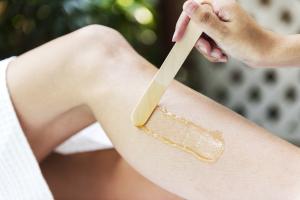 Photo épilation jambes cire spa : esthéticienne applique bande cire chaude demi-jambe face avant, geste professionnel arrachage poils inverse pousse, peau lisse soyeuse.