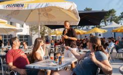 Jeu SOL'APERO avec un animateur qui pose des questions aux résidents lors de leur pause de fin de journée ensoleillée avec les parasols jaunes de la marque Pelforth