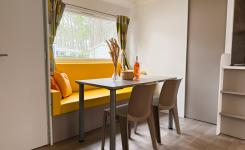 Vue intérieure du coin repas et salon avec canapé d'un mobil home au camping familial en bord de mer dans les Landes, avec environnement verdoyant