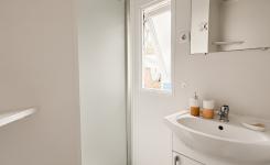 Salle de bain avec douche et lavabos et rangements aux murs blancs dans un mobil home spacieux avec vue sur la nature et la mer dans les Landes
