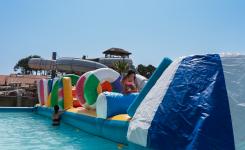Animation de jeu aquatique Total Wipe Out pour les enfants et adolescents au camping Le Vieux Port à Messanges, comprenant une grande aire avec des obstacles gonflables flottants, des ponts suspendus, des trampolines, et des bouées, offrant une activité ludique, sportive et rafraîchissante en plein air sous un ciel ensoleillé