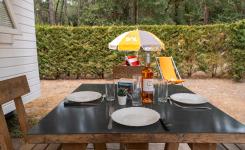 Espace extérieur du mobil-home Eco 4 personnes avec table et chaises en bois pour tous les repas de vacances dans un camping des Landes