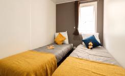 Chambre avec lits duo, plaids couleur jaune et oreillers bleu et blanc, pièce lumineuse idéale pour faire dormir les enfants et vivre un maximum en extérieur pour des vacances inoubliables