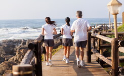 Course à pied en face de la plage avec 3 personnes de dos faisant leur jogging sur un accès en bois en face de l'océan en bord de mer